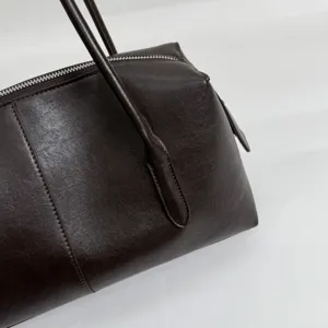 Detalle del bolso marrón oscuro: textura tipo piel, costuras visibles, cremallera y asa fina