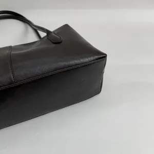 Primer plano de la base texturizada del bolso oscuro de cuero sintético, con costura lateral y asa