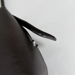 Primer plano de la superficie de cuero marrón oscuro, con correa fina y detalle del cierre plateado