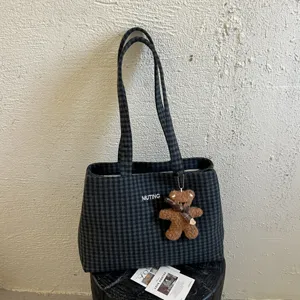 Navy and gray plaid tote with long straps and a brown plush bear charm, shown hanging