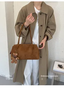 Modelo sostiene un bolso marrón de ante con un pequeño colgante de osito ante una pared clara