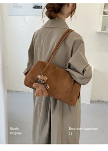 Vista trasera de un bolso marrón de ante, con dos correas largas y un osito de peluche colgante