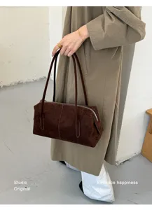 Detalle de una persona con bolso bandolera de ante marrón, asas largas y cierre con cremallera