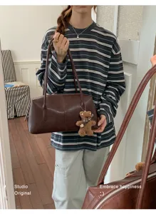 Una persona lleva un bolso marrón con un pequeño colgante de osito de peluche visible