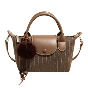 Vue de face d’un sac rayé effet tweed, avec rabat en similicuir brun, pompon et breloque chaîne