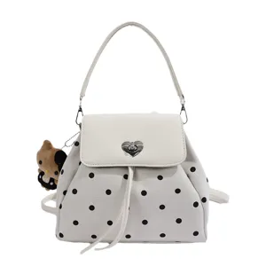 Front view of a white polka-dot bag with a heart clasp, shoulder strap, and plush bear charm
