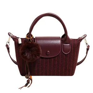 Vue de face d’un sac tissé bordeaux à rayures, avec bordure similicuir, anses, pompon et pampille