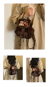 Brown suede backpack worn by a model, featuring a teddy bear patch and flap closure