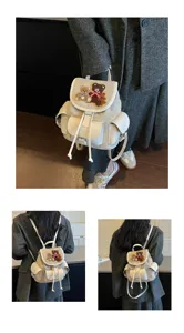 Model wearing a cream backpack with teddy bear embroidery, drawstring closure and flap pockets