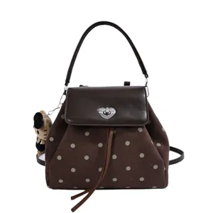 Front view of a brown polka-dot bag with a leather flap, heart-shaped clasp and plush bear charm