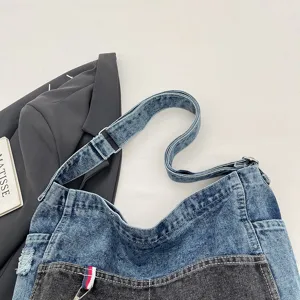 Flat lay of a washed denim bag with light blue and charcoal panels and an adjustable strap.