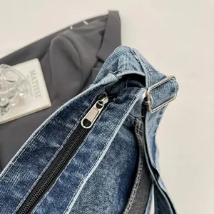 Close-up of the washed denim bag's black zipper, silver pull, and adjustable strap buckle.