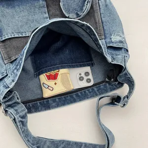 Top-down view inside a washed denim bag, showing a dark inner pocket, zipper and phone