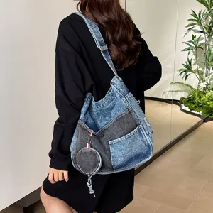 Model wearing a blue and charcoal denim shoulder bag with a wide strap, front pockets and coin pouch