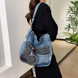 Model wearing a blue and charcoal denim shoulder bag with a round coin purse charm and tassel.