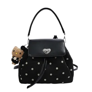 Front view of a black polka-dot bag with a heart clasp, tassel detail, and teddy bear charm