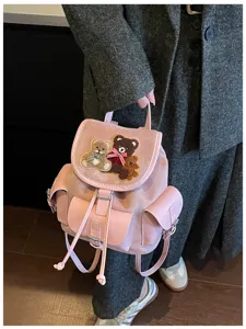 Pink backpack shown in hand, with teddy bear appliqués, a red plaid bow and drawstring pockets