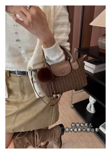 Modella con borsa marrone a righe, patta e manici in pelle, pompon e nappa, in ambiente interno