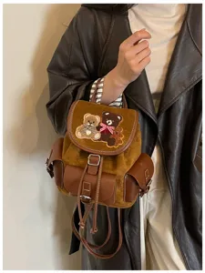 Close-up of teddy bear embroidery on a brown suede flap, with leather trim and drawstring cords