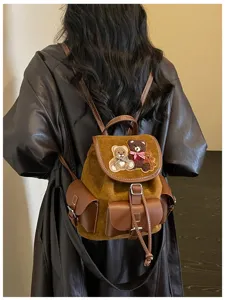 Rear view of a model wearing a brown suede backpack with teddy bear patches and a leather flap