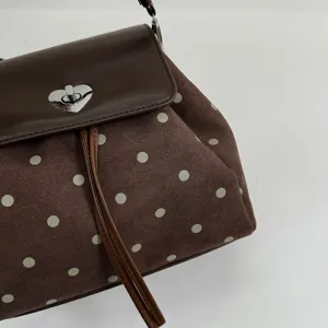 Close-up of pale green dots on brown suede, with a leather flap and silver heart-shaped clasp