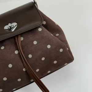 Close-up of cream dots on brown suede, with a dark leather flap and silver turn-lock clasp