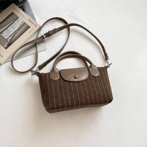 Sac marron en tissu rayé posé sur une table blanche, avec rabat en similicuir et longue bandoulière