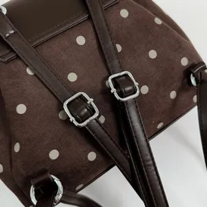 Close-up of brown suede with pale polka dots, dark leather-look straps, and silver buckles