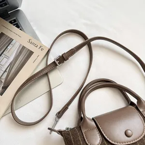 Détail d’un sac brun en tissu rayé, avec rabat en cuir, bouton-pression et bandoulière réglable