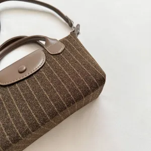 Gros plan sur le tissu brun à fines rayures, le rabat et la poignée en similicuir, avec bandoulière
