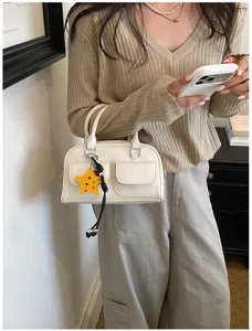 Borsa bianca con tasche a patta e ciondolo a stella gialla, indossata con un maglione beige