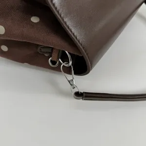 Close-up of silver metal clasp and rings connecting a brown dotted bag to its shoulder strap
