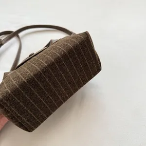 Gros plan sur le tissu rayé brun du sac, sa bandoulière en cuir foncé et ses détails métalliques