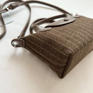 Gros plan sur un sac en suédine marron à rayures, avec anse en cuir et détails métalliques.