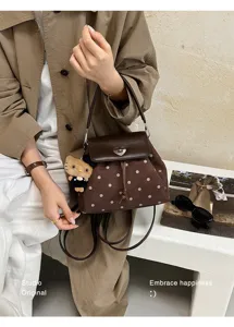 Brown polka-dot suede-look bag with heart clasp and teddy charm, shown on a model
