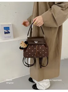 A person holds a brown dotted suede bag with leather flap, drawstring closure and teddy charm