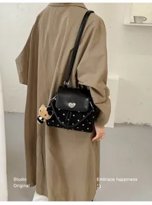Rear view of a model wearing a black dotted bag with heart clasp and plush bear charm