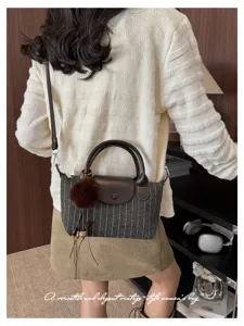 Vista posteriore di una borsa grigia a righe sottili, con patta e manico in pelle marrone e pompon