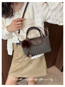 Borsa a righe grigie con patta in pelle marrone e pompon, mostrata indossata con un outfit chiaro