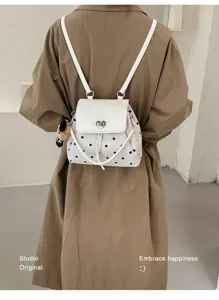 Back view of a white polka-dot backpack with heart clasp and teddy charm worn over a tan coat