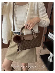 Dettaglio di una borsa a righe marroni con patta in pelle, manici, tracolla e pompon morbido