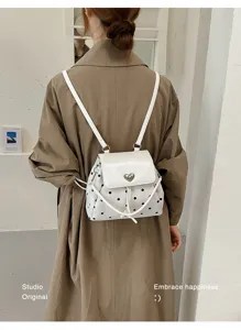 Rear view of a white backpack with black dots, heart-shaped clasp and adjustable shoulder straps