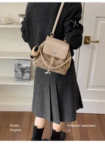 Model wearing a beige dotted suede-look bag with a heart-shaped metal clasp and bear charm