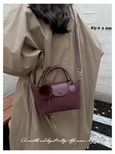 Borsa a righe bordeaux indossata a spalla, con patta in pelle, manici e pon pon decorativo