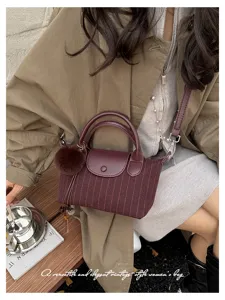Dettaglio di una borsa bordeaux a righe, con patta in similpelle, manici e pompon morbido