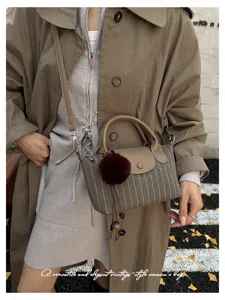 Borsa a righe con patta marrone, manici curvi, pompon e nappa, indossata con cappotto neutro