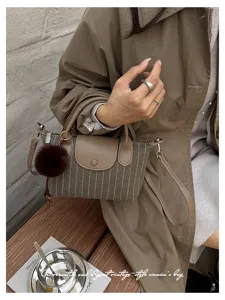 Dettaglio di una donna con borsa a righe, patta marrone, pon pon in finta pelliccia e tracolla