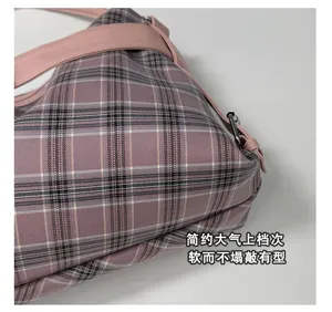 Close-up detail of pink plaid fabric, a faux-leather strap and silver-tone bag hardware
