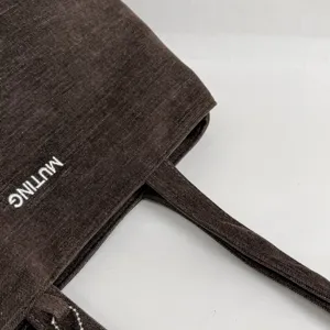 Primer plano de tejido marrón oscuro, asa a juego y letras blancas bordadas en la bolsa