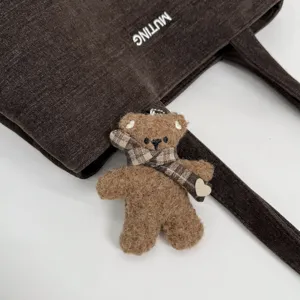 Primer plano de un bolso marrón oscuro texturizado con osito de peluche, bufanda de cuadros y corazón